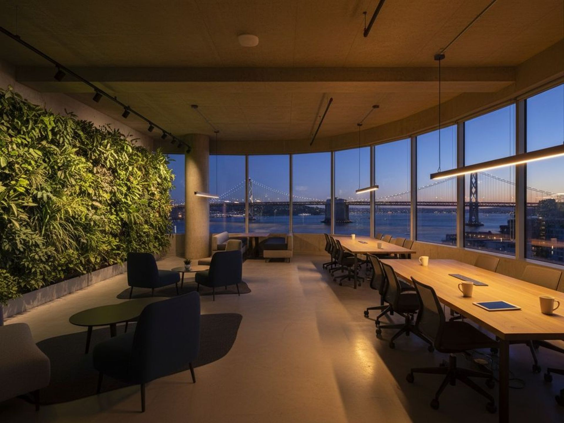 Sleek modern co-working space with exposed concrete, living wall of plants, and panoramic bay windows showing San Franci